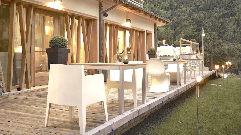 Mūsdienīga terase ar baltiem galdiem un krēsliem, apkārtne ar koku foniem un silto apgaismojumu, radot relaksējošu atmosfēru.