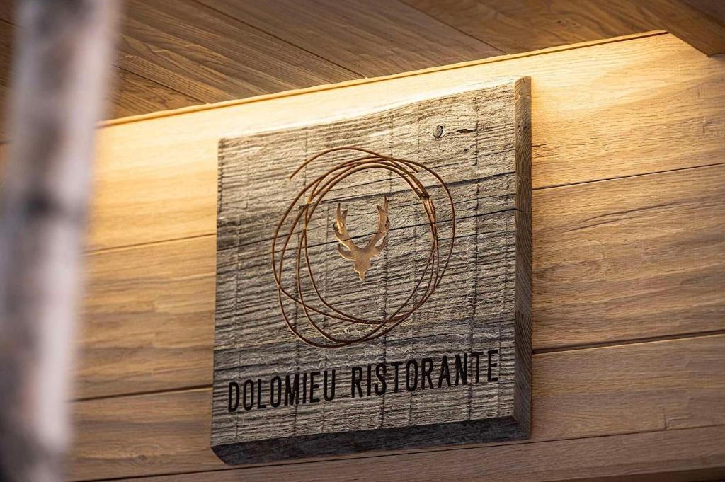 Koka zīme ar nosaukumu "Dolomieu Ristorante", dekorēta ar stilizētu staltbrieža attēlu un apvīto līniju, kas piešķir modernu izskatu.