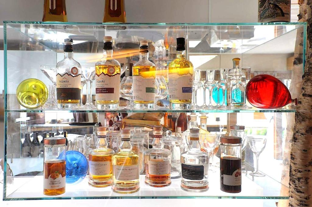 Stikla vitrīnā izvietoti dažādi dzērieni un glāzes, ieskaitot vairākas pudeles ar viskiju un krāsainas stikla dekorācijas.