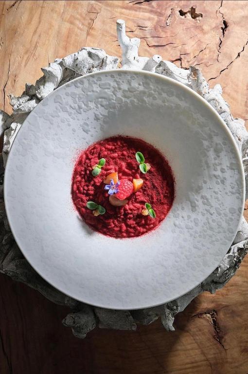 Sarkans desertu ēdiens ar dekoratīvām sastāvdaļām, pasniegts balta šķīvī uz koka virsmas.