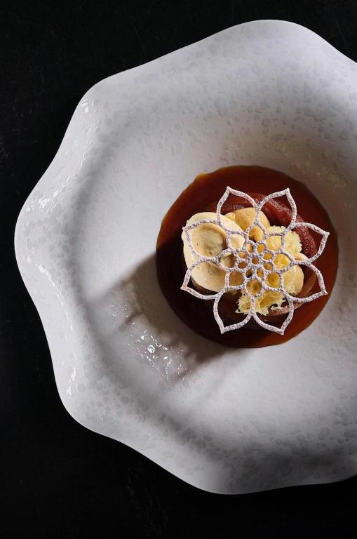 Elegants deserts ar krēmveida virsotni un izsmalcinātu rotājumu, pasniegts uz viļņota formas šķīvja.