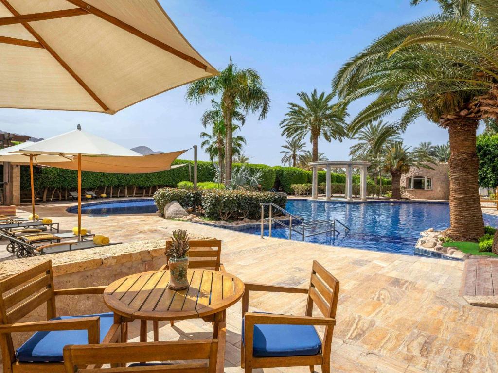 Atpūtas zona ar baseinu un palmu kokiem, kur ir koka galds un krēsli. Zem saulessarga ir atpūtas krēsli, kas gaida viesus. Ideāla vieta relaksācijai un atpūtai.