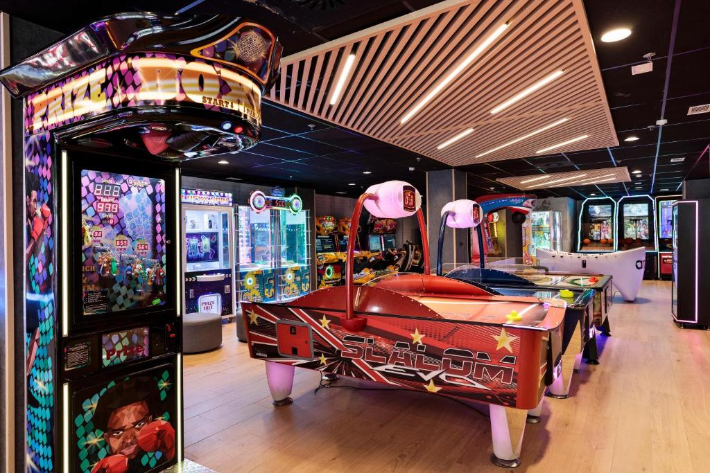 Spēļu zāle ar dažādiem arcade spēļu automātiem, tostarp gaisa hokeja un prēmiju spēlēm, kas piedāvā krāsainus gaismas efektus un jautras izklaides iespējas.