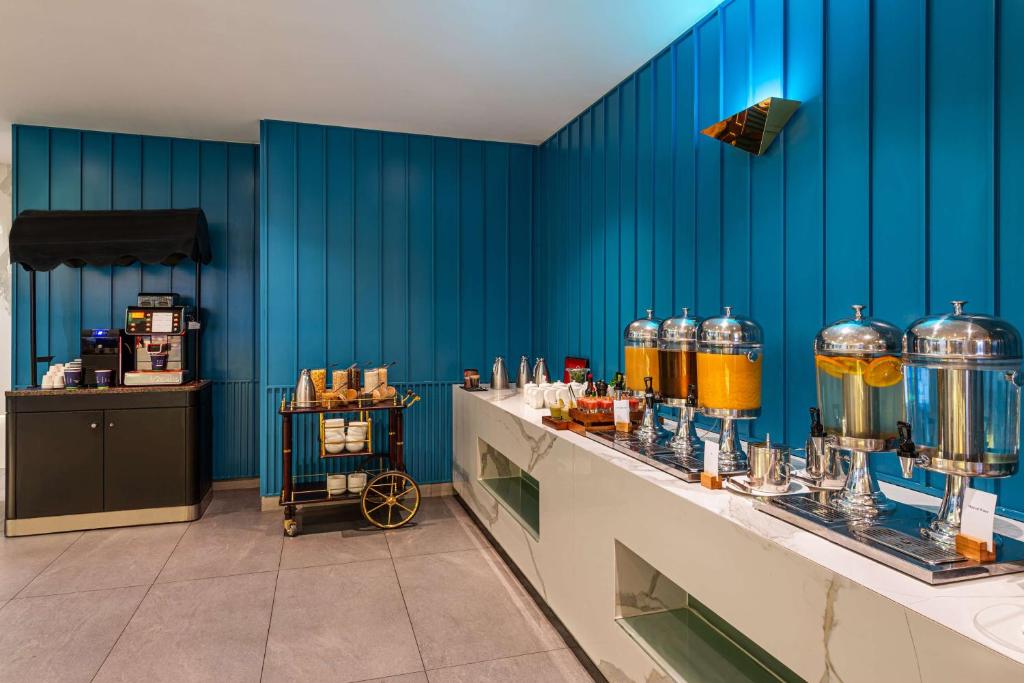 Moderns bufetes stūris ar dzērienu dozatoriem un kafijas automātu, uzsverot zilu sienu un elegantu interjeru.