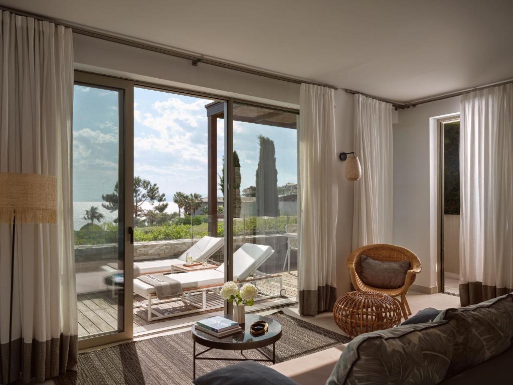 Mūsdienīgs viesistabas interjers ar plašu skatu uz jūru, kurā ir ērta mēbele un dabiska apgaismojuma elementi. Dūmakaini toņi un augu akcenti rada relaksējošu atmosfēru.