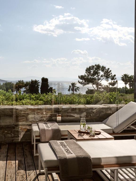 Mūsdienīgs atpūtas laukums ar sauļošanās krēsliem un galdiņu, kas piedāvā skatu uz jūru un dabu, radot relaksējošu atmosfēru.