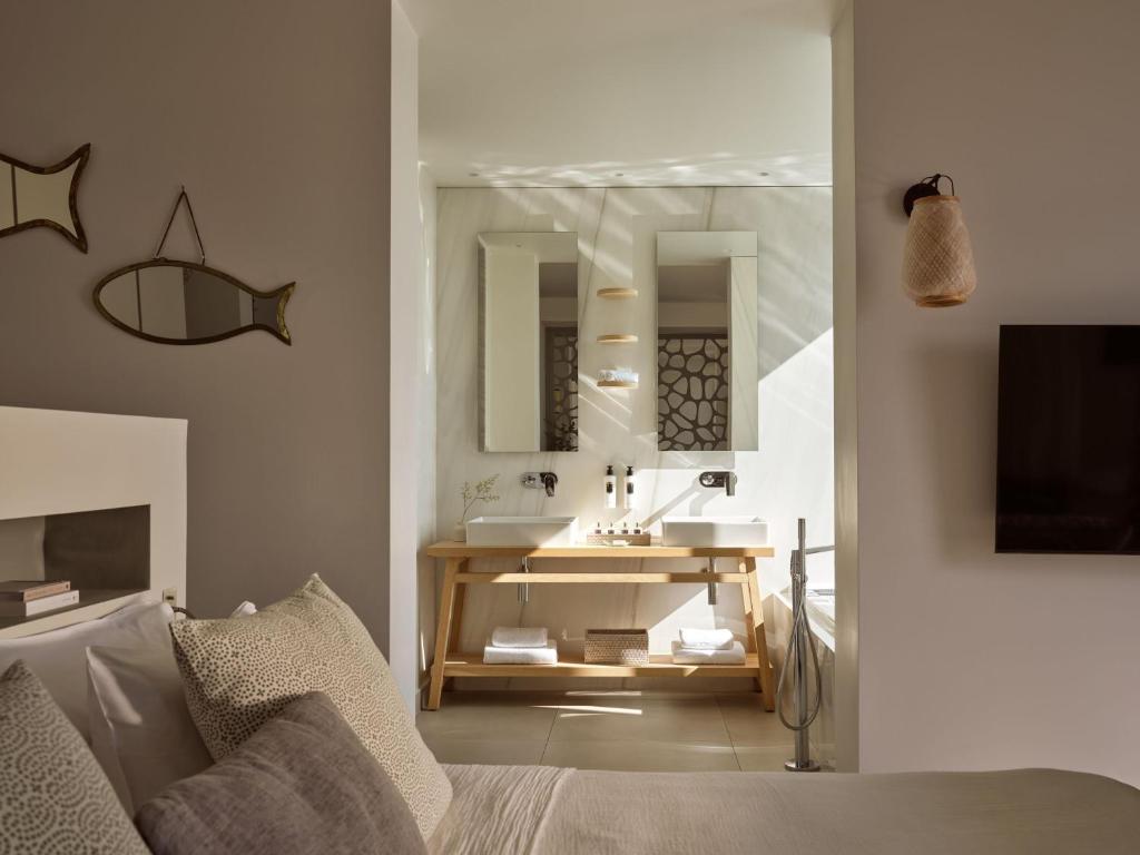 Mūsdienīgs guļamistabas interjers ar vannasistabu, kurā ir divi spoguļi un koka izlietne. Sienās ir dekoratīvi elementi, un telpā ieplūst dabiska gaisma.