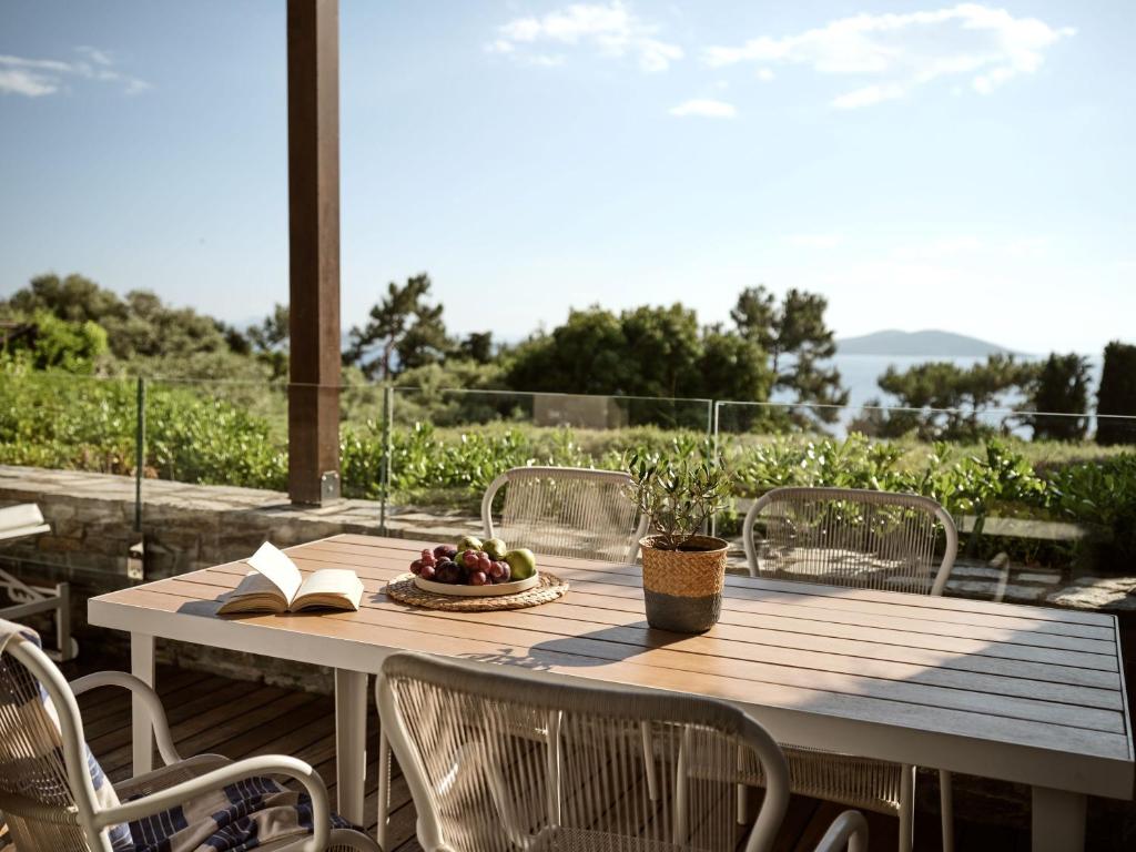 Mūsdienīga terase ar skatu uz dabu, kurā ir galds ar augļiem un grāmatu, radot relaksējošu atmosfēru. Ideāla vieta atpūtai un baudīšanai.