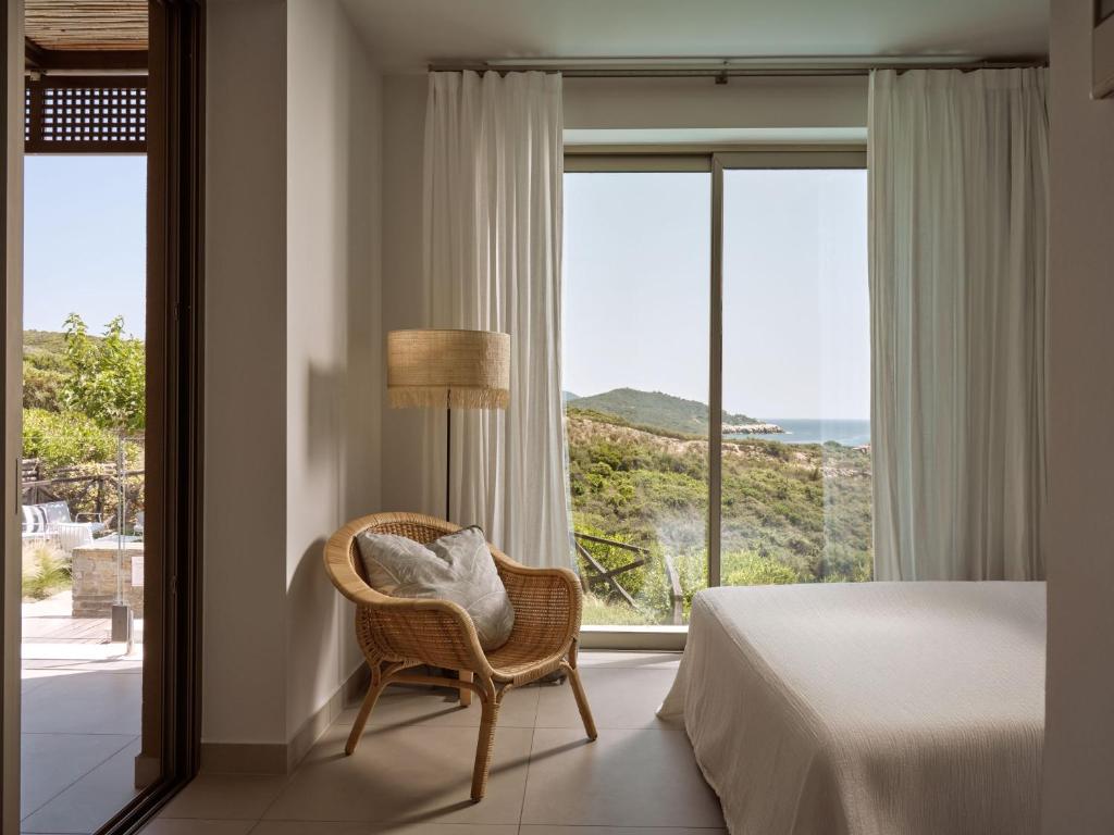 Mūsdienīgs guļamistabas interjers ar skatu uz dabu, ietverot vīnogulāju un jūras ainavu, kā arī ērta vāku krēsla un gaismas avota elementus.