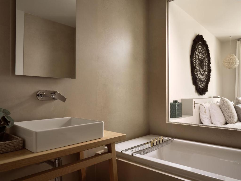 Moderns vannas istabas dizains ar minimālistisku izskatu, kurā iekļauts baltas keramiskās izlietnes un koka galds, kā arī eleganta vannas istabas zona.