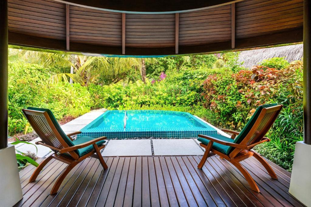 Relaksējoša ainava ar divām koka krēslām, kas vērsti uz privātu baseinu un sulīgu dārzu. Ideāla vieta atpūtai un atpūtas brīžiem.