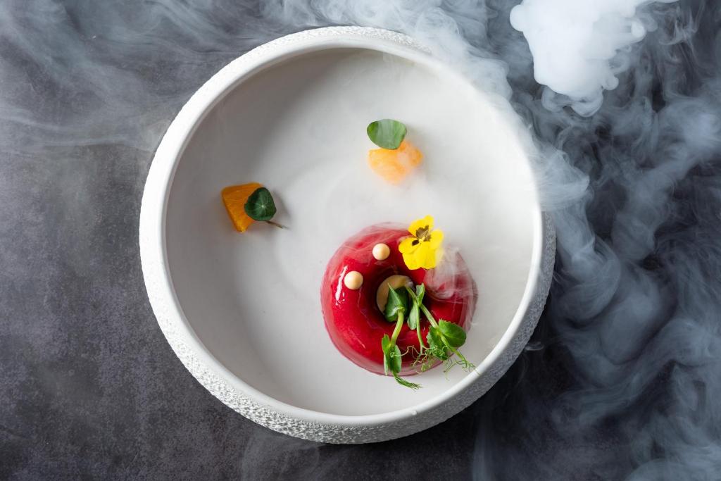 Sarkans deserts ar ziediem un augļiem, kas pasniegts mākslinieciskā šķīvī ar dūmiem.
