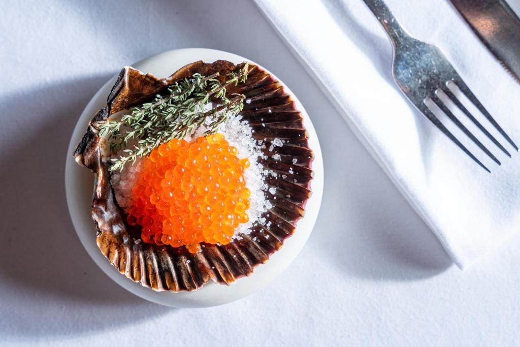 Svaigu jūras veltes pasniegšana uz šķīvja, kurā ir jūras gliemežvāks ar oranžām ikriem un garšaugiem, papildināts ar sāli.