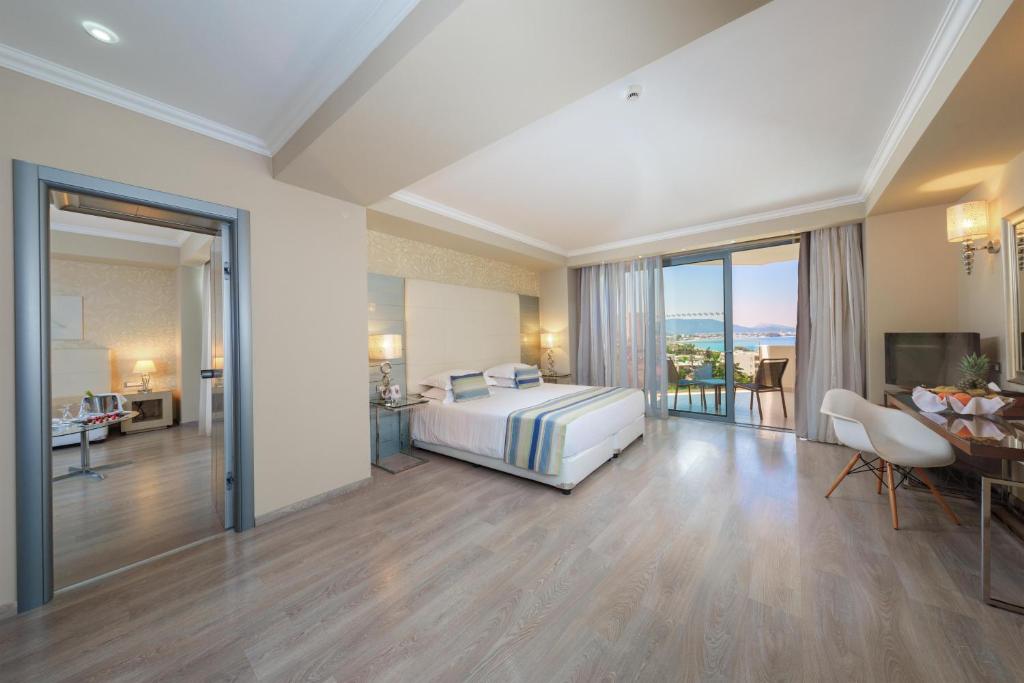 Moderns viesnīcas numurs ar plašu logu, no kura paveras skats uz jūru, un elegantu interjeru, kas ietver gultu un atpūtas zonu.