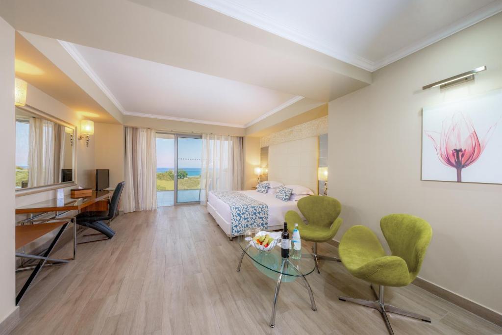 Mūsdienīgs viesnīcas numurs ar plašu skatu uz jūru, iekārtots ar divguļamo gultu, dīvānu un galdu. Telpā ir moderni zaļi krēsli un eleganta dekorācija.