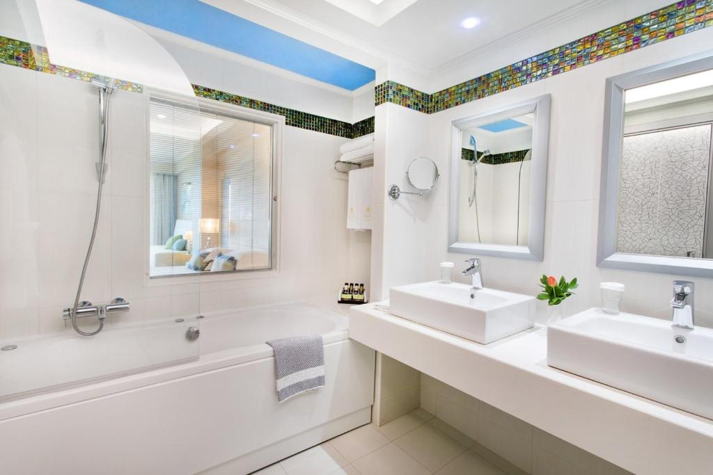 Mūsdienīgs vannas istabas interjers ar divām izlietnēm, vannu un stikla dušu, papildināts ar krāsainu mozaīku un mūsdienīgām spoguļiem.