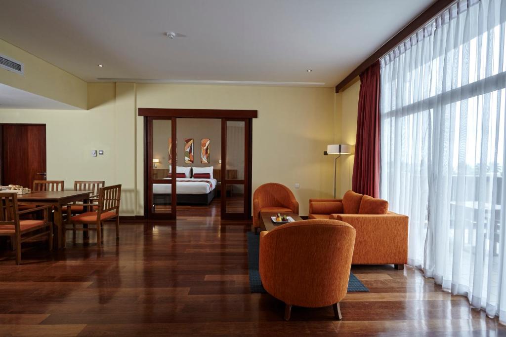Moderns viesnīcas numurs ar elegantu interjeru, kurā ir ērtas oranžas krēsli un liels galds. Logi nodrošina dabīgu apgaismojumu un skatu uz ārpusi.