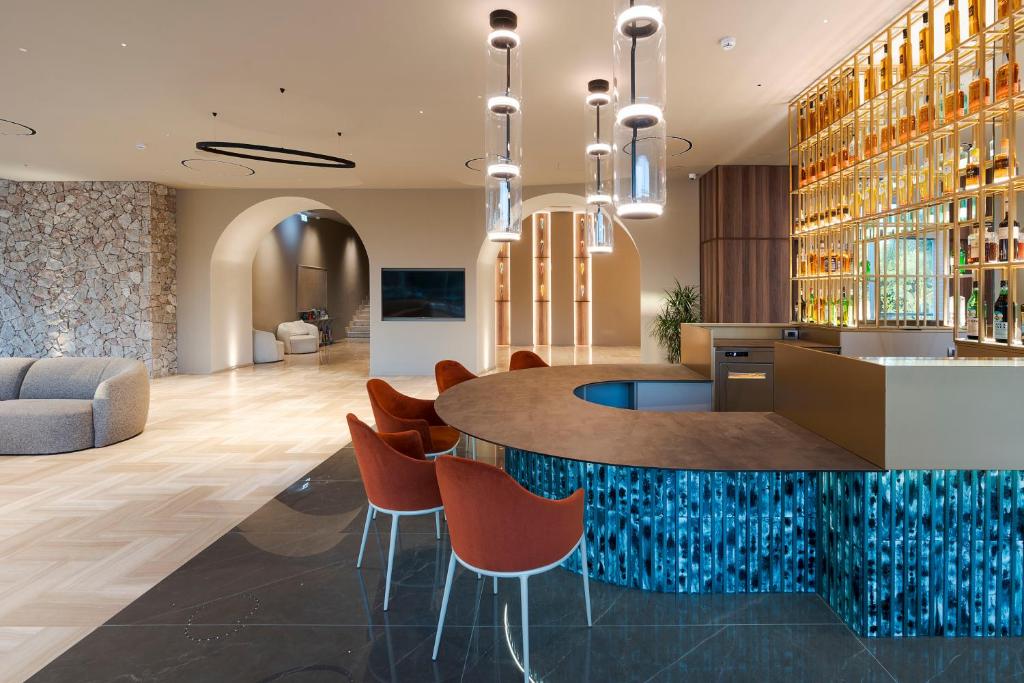 Mūsdienīgs viesnīcas bārs ar elegantām sarkanām krēsliem un izsmalcinātu interjeru, kas ietver akmens sienu un izstādītu dzērienu plauktu.