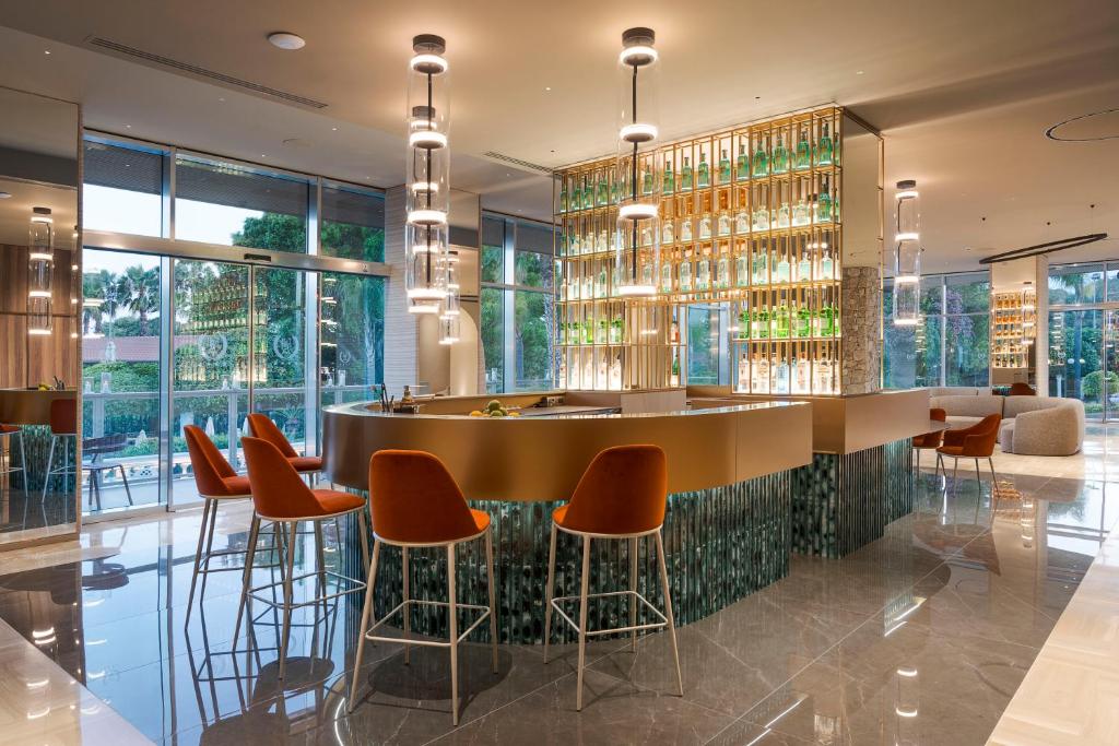 Mūsdienīgs bārs ar elegantu dizainu, apgaismots ar stilīgām lampām un dekoratīvu alkoholisko dzērienu plauktu. Interjers ir plašs un gaišs, nodrošinot komfortablu atmosfēru.