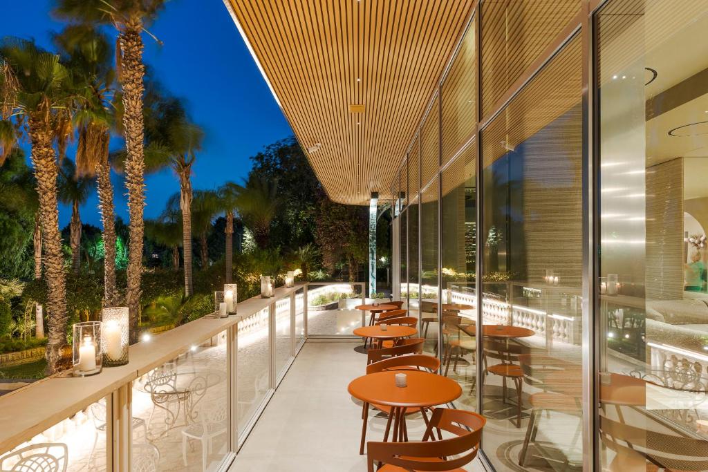 Mūsdienīgs terases dizains ar oranžiem galdiem un palmām, kas izceļas vakarā, apgaismojot apkārtni. Ideāla vieta relaksācijai un baudīšanai.