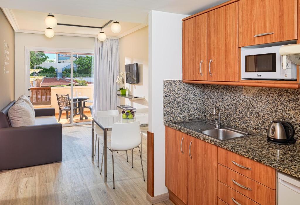 Mūsdienīga virtuve ar koka skapīšiem, granīta virsmām un ēdamzonu, kurā ir galda un krēsli. Skats uz āra terasi ar mēbelēm.