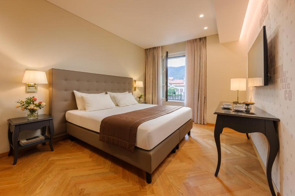 Mūsdienīga un eleganta viesnīcas guļamistaba ar divguļamo gultu, siltām krāsām un dabisku apgaismojumu. Interjerā ir iekļauti dekoratīvi elementi, piemēram, naktsgaldiņš un televizors.