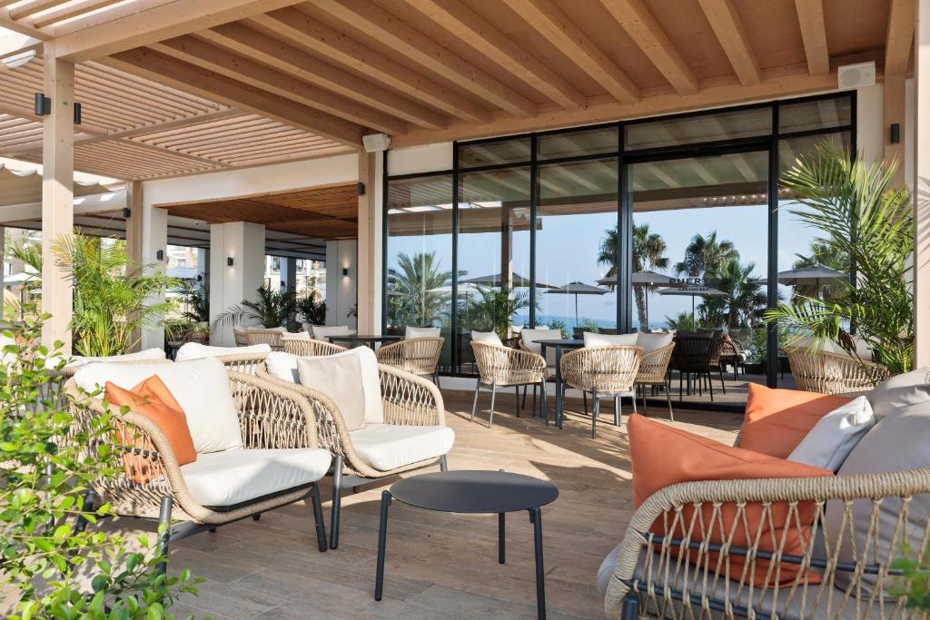 Mūsdienīgs terases interjers ar ērtām ratiņu mēbelēm, zaļām palmām un skatu uz jūru. Ideāla vieta relaksācijai un atpūtai.