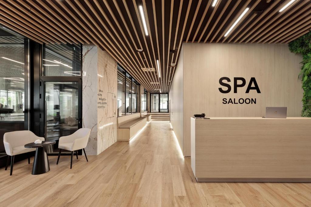 Mūsdienīgs SPA salona interjers ar koka grīdu, gaišām sienām un relaksējošu atmosfēru. Reģistratūras zona ar elegantu dizainu un augu elementiem.