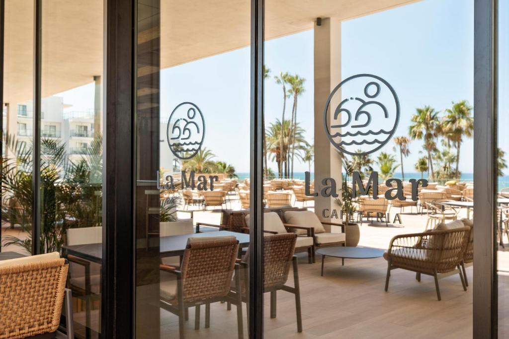Restorāna "La Mar" logotips redzams caur stiklu, kas atspoguļo pludmales skatu ar palmām un terasi.