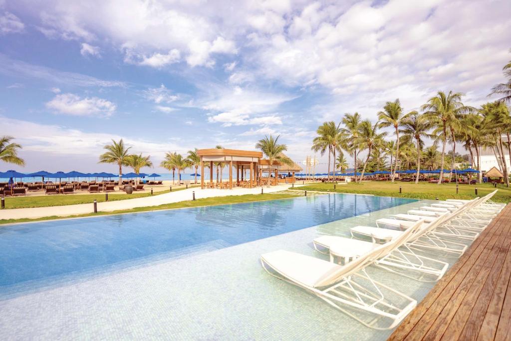 Angsana Laguna Phuket baseins ar palmām un atpūtas krēsliem piekrastē