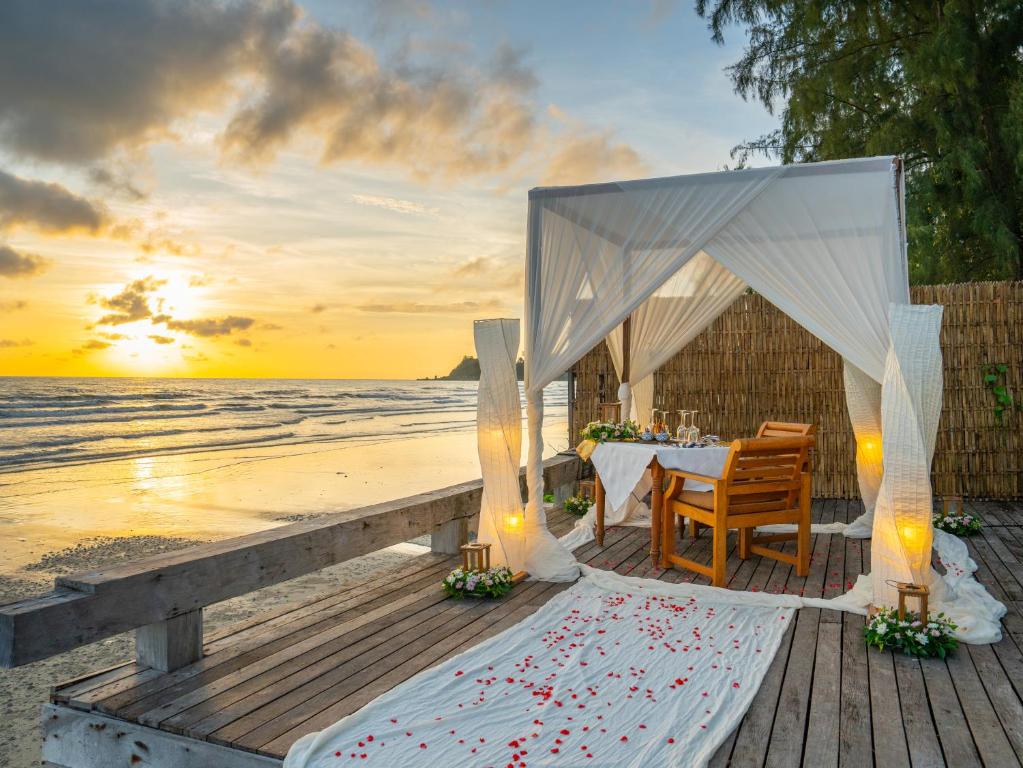 Romantisks pludmales restorāns ar saulrietu fona, rotāts ar ziedlapiņām un mīkstiem gaismas avotiem. Ideāla vieta romantiskām vakariņām pie jūras.