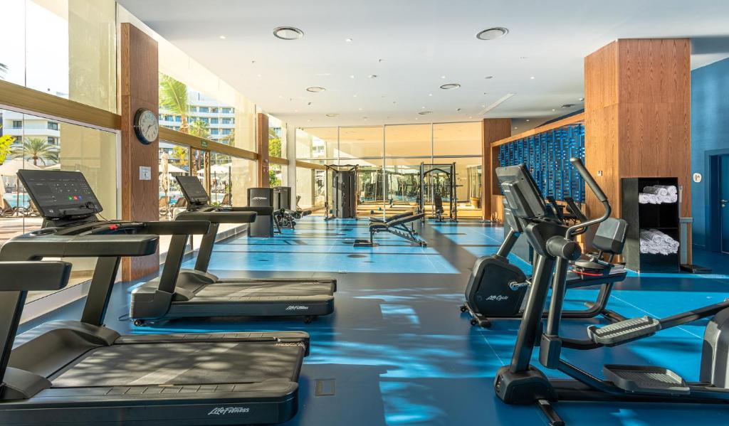 Mūsdienīga sporta zāle ar skatu uz ārpusi, aprīkota ar skrejceliņiem un citiem trenažieriem, ideāla vieta treniņiem un veselīga dzīvesveida uzturēšanai.