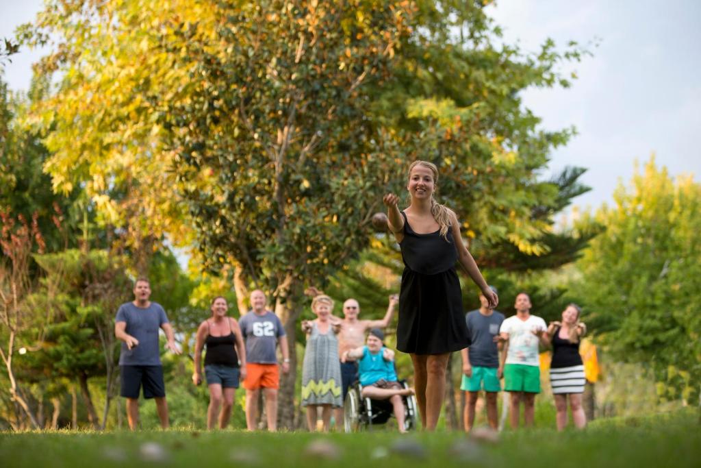 Grupas cilvēku izklaide dabā, kad jaunā sieviete spēlē spēli, turēdama rokās objektu. Apkārt viņai ir smaidoši cilvēki, kas atbalsta viņu. Fons ir zaļš ar koku un saulainu laiku.