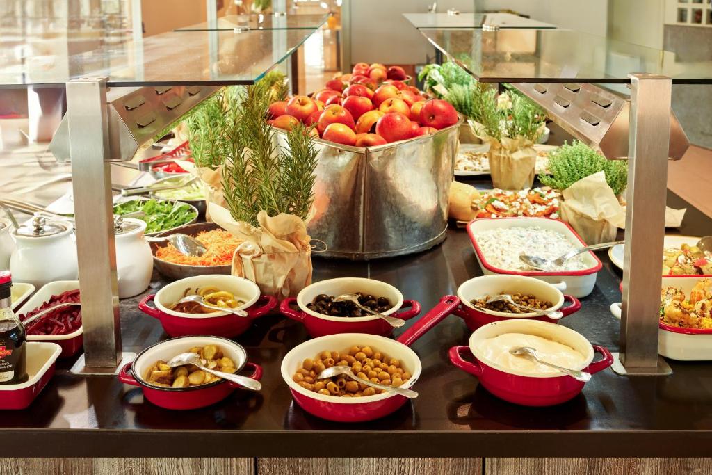Daudzveidīgs bufete ar svaigiem augļiem, dārzeņiem un dažādām uzkodu opcijām, kas pasniegtas elegantos traukos. Pievilcīgs ēdienu klāsts, kas iepriecina garšas kārpiņas.