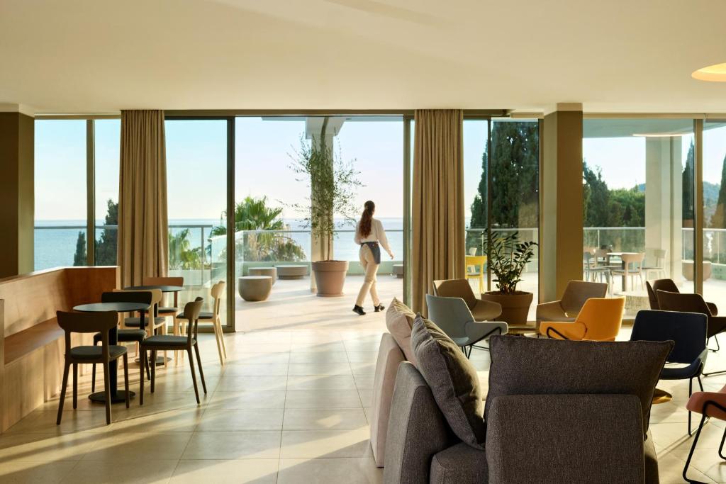 Lielisks mūsdienīgs viesnīcas interjers ar plašiem logiem un skatu uz jūru, kurā redzami eleganti mēbeļu komplekti un gaisīgs atmosfēra.