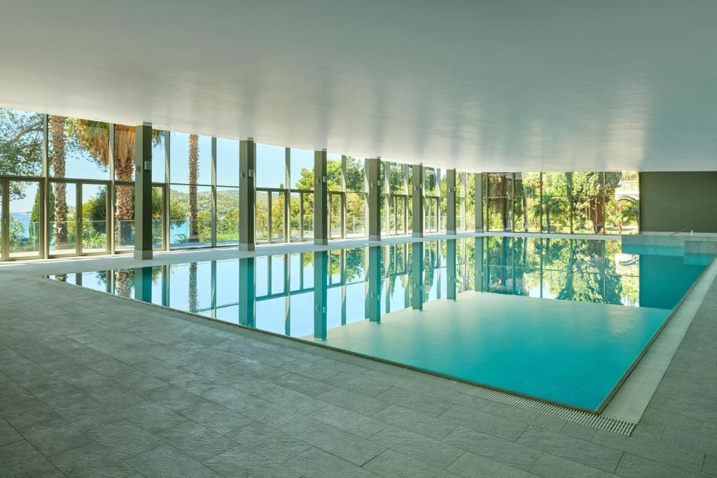 Moderns iekštelpu peldbaseins ar lieliem logiem, caur kuriem redzams apzaļumots ainavas skats. Gaisīgs un elegants dizains nodrošina relaksējošu atmosfēru.