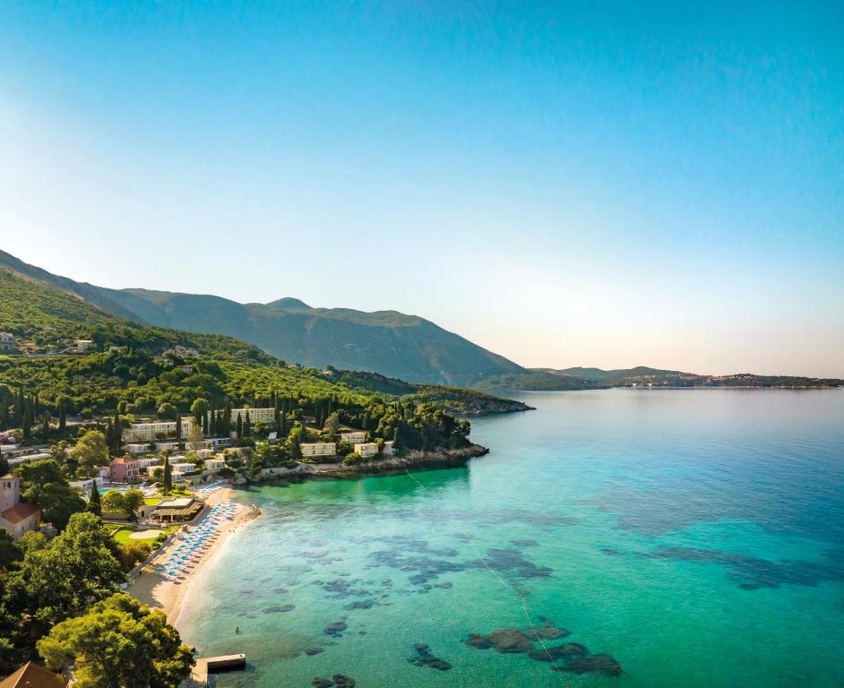 Skaists piekrastes skats ar pludmali, kas apņem skaidru zilo ūdeni un kalnu ainavu, ideāli piemērots atpūtai un brīvdienām.