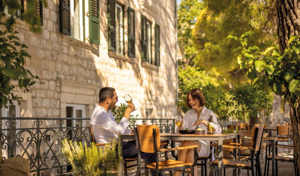 Pāris baudīja maltīti ārpusē, sēžot pie galda restorānā ar zaļām lapām un akmens sienām. Gaisā ir relaksējoša atmosfēra, kas liek justies kā atpūtai.