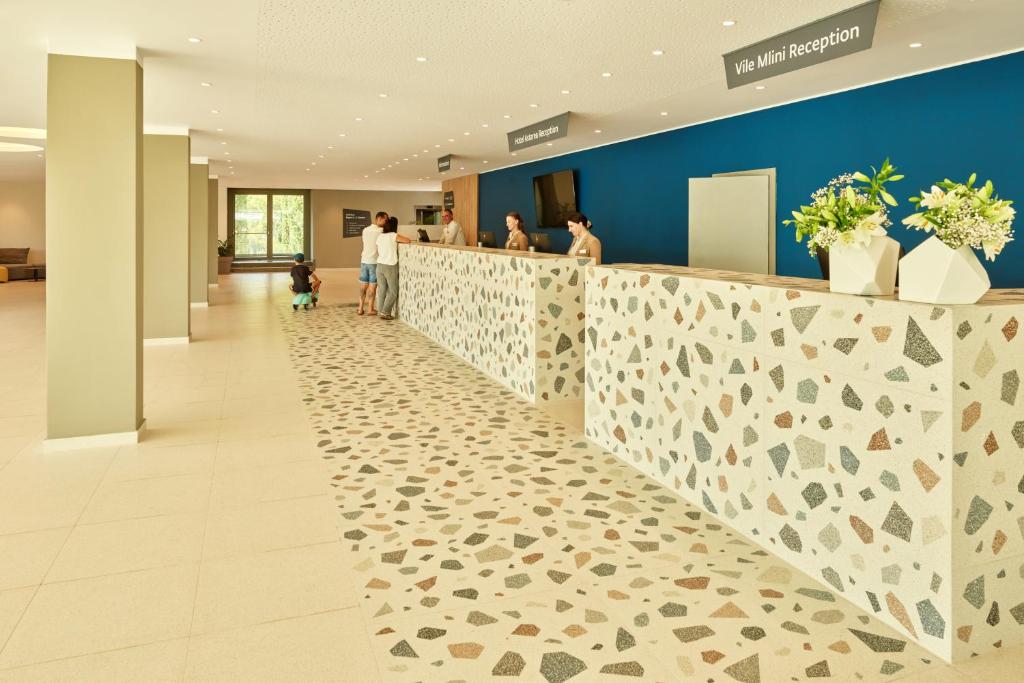 Moderns viesnīcas reģistrācijas stends ar akmens grīdu un ziedu dekorācijām, kur viesi saņem pakalpojumus.