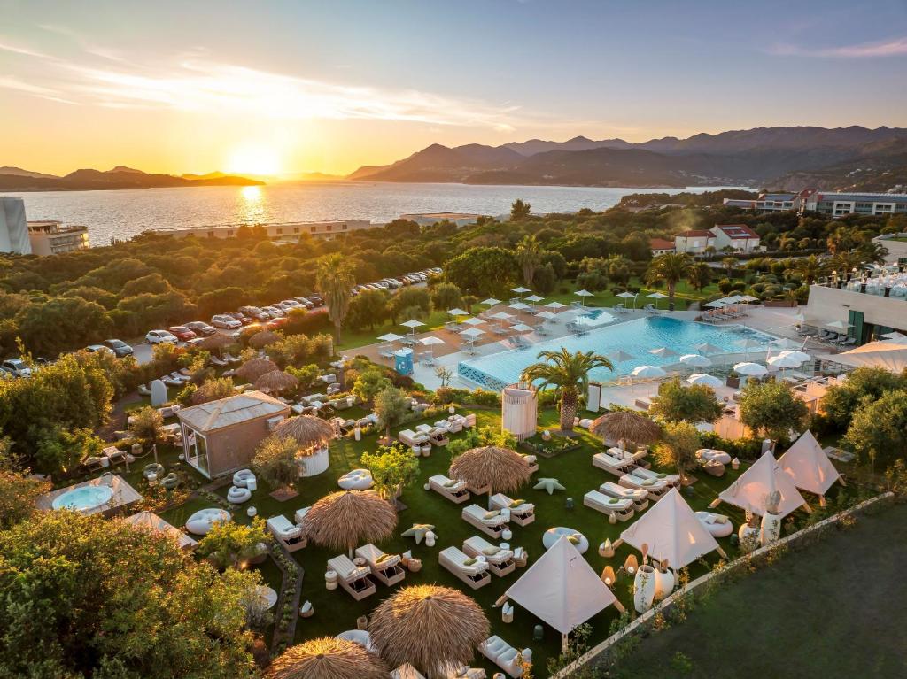 Saulrieta skats uz luksusa viesnīcu ar baseinu, palmām un atpūtas zonām. Apkārt ir zaļumi un līcis.