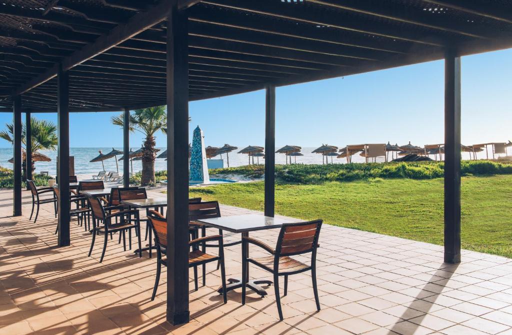 Jauka terase ar skatu uz jūru, kurā ir galdi un krēsli, apzaļumota zāle un pludmales lietussargi. Ideāla vieta relaksācijai un atpūtai pie ūdens.