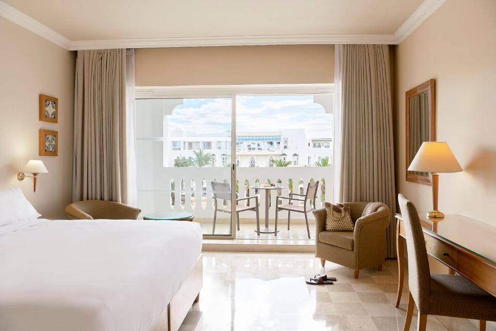 Mūsdienīga viesnīcas numura interjers ar gaišām krāsām, kurā ir liels logs, kas ved uz balkonu. Numurā ir ērta gulta, dīvāns, rakstāmgalds un gaismas avots.