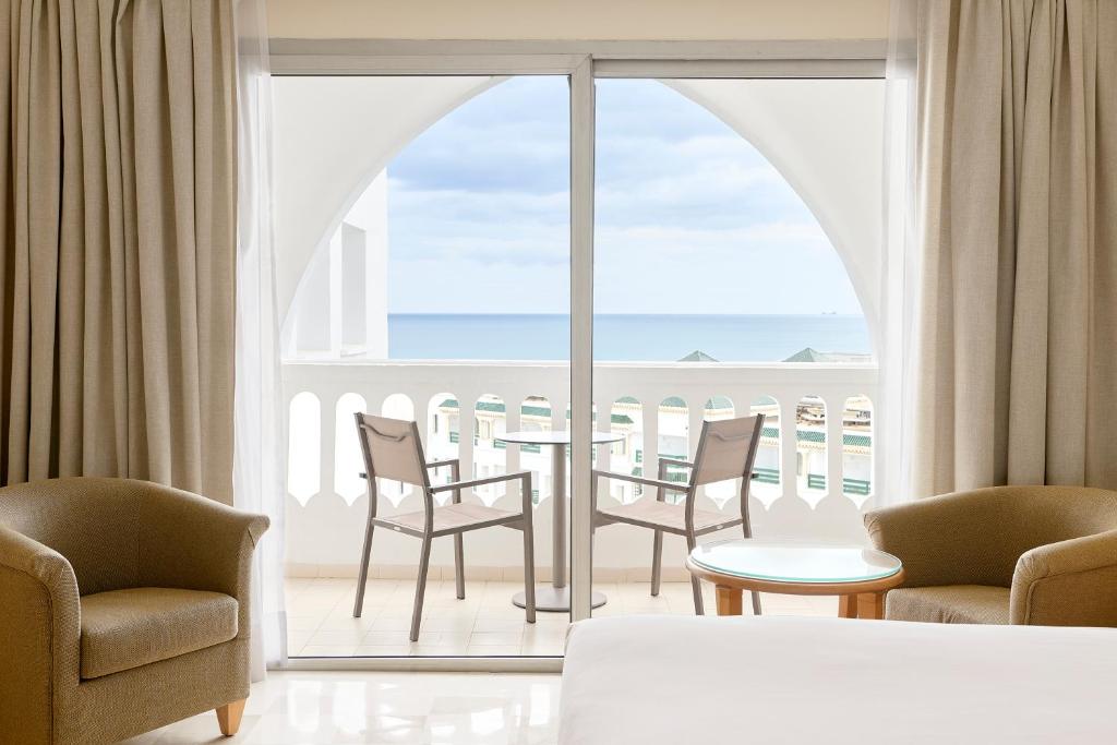 Mūsdienīgs viesnīcas numurs ar plašu skatu uz jūru, gaišām aizkariem un diviem ērtajiem krēsliem uz balkona. Ideāla vieta relaksācijai un atpūtai.
