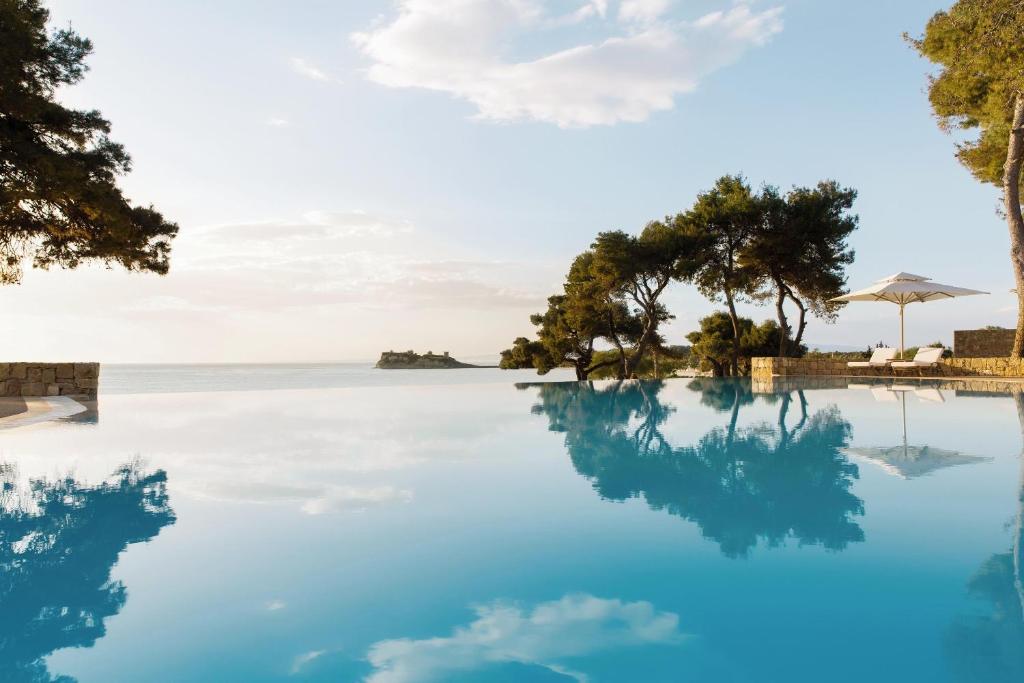 Mūsdienīgs baseins ar kristāldzidru ūdeni, kas atspoguļo debesu un apkārtējās dabas skaistumu, blakus zaļiem kokiem un pludmales guļamkrēsliem. Ideāla vieta relaksācijai un atpūtai.