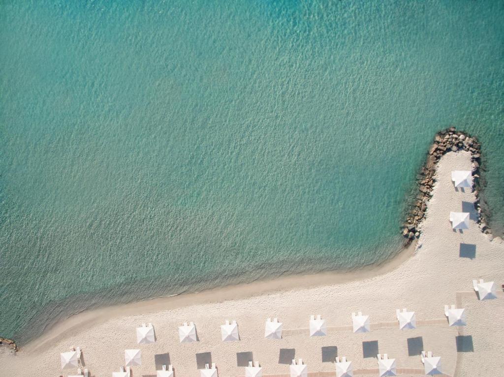 Skaista pludmales ainava ar baltām saulessargiem un kristāldzidru ūdeni. Pludmale ir klāta ar smiltīm, veidojot mierīgu atmosfēru.