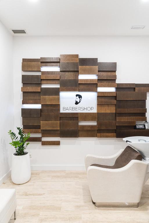 Mūsdienīgs frizētavas interjers ar koka paneļiem un melnu "BARBERSHOP" zīmi, pie kura atrodas augu pods un ērta krēsls.