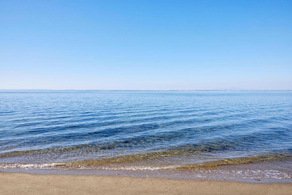Mierīga jūra ar skaidru zilu debesi un smilšu krastu, radot relaksējošu un idillisku ainavu.