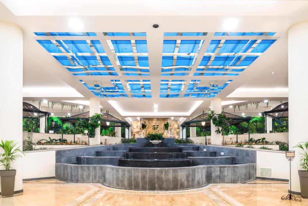 Mūsdienīgs iekštelpu ūdens strūklaka ar zilu stikla griestu dizainu, kas iegriežas zaļajos augos un elegantā arhitektūrā. Ideāla vieta relaksācijai un atpūtai.