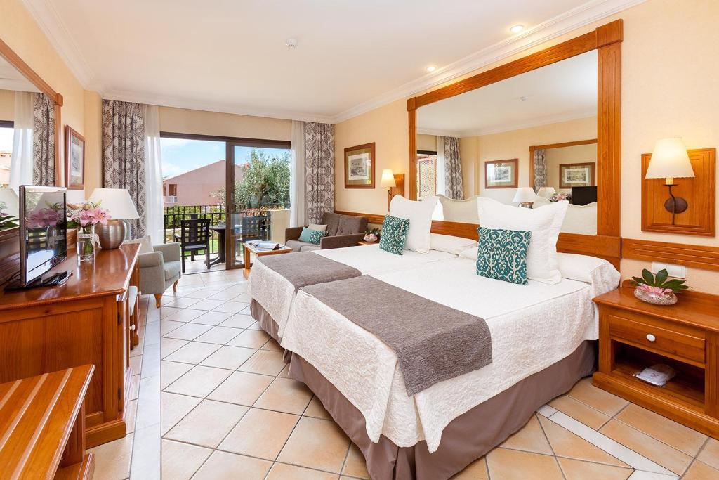 Luksusa viesnīcas numurs ar divām gultām, modernu interjeru un balkonu, no kura paveras skats uz dārzu. Telpā ir arī dīvāns un televizors, radot ērtu un mājīgu atmosfēru.