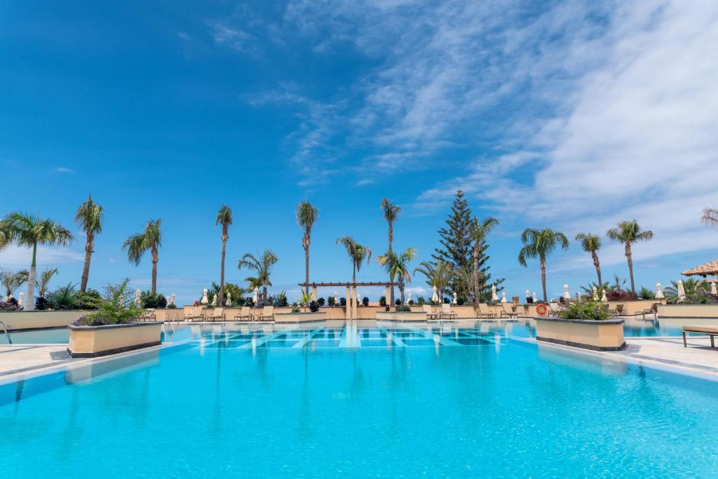Lielisks baseins ar palmām un zilu debesu fonu, radot atpūtu un relaksāciju. Ideāla vieta atpūtai pie ūdens.